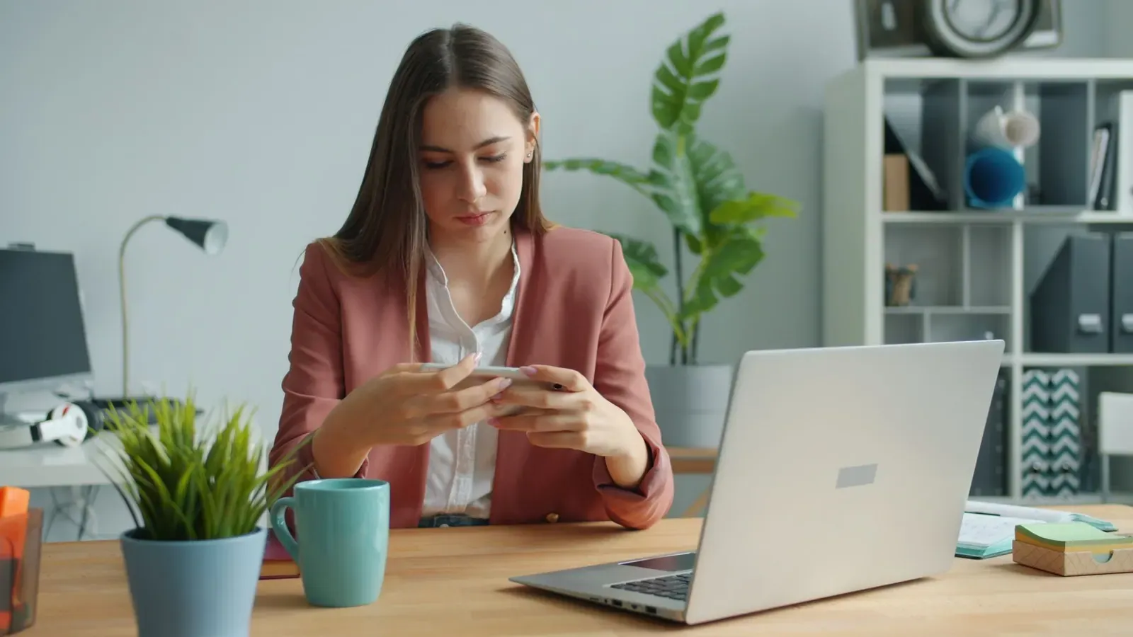 Femme à son bureau consultant son smartphone devant son ordinateur portable