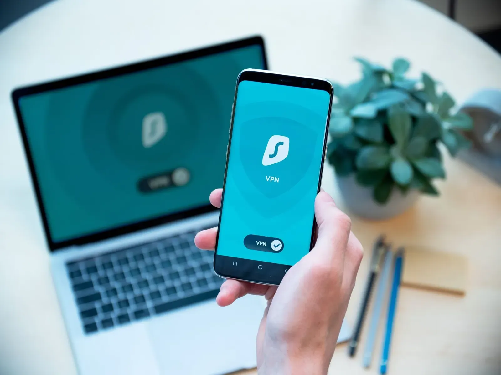 Gros plan sur une main tenant un smartphone avec une application VPN, ordinateur portable en arrière-plan