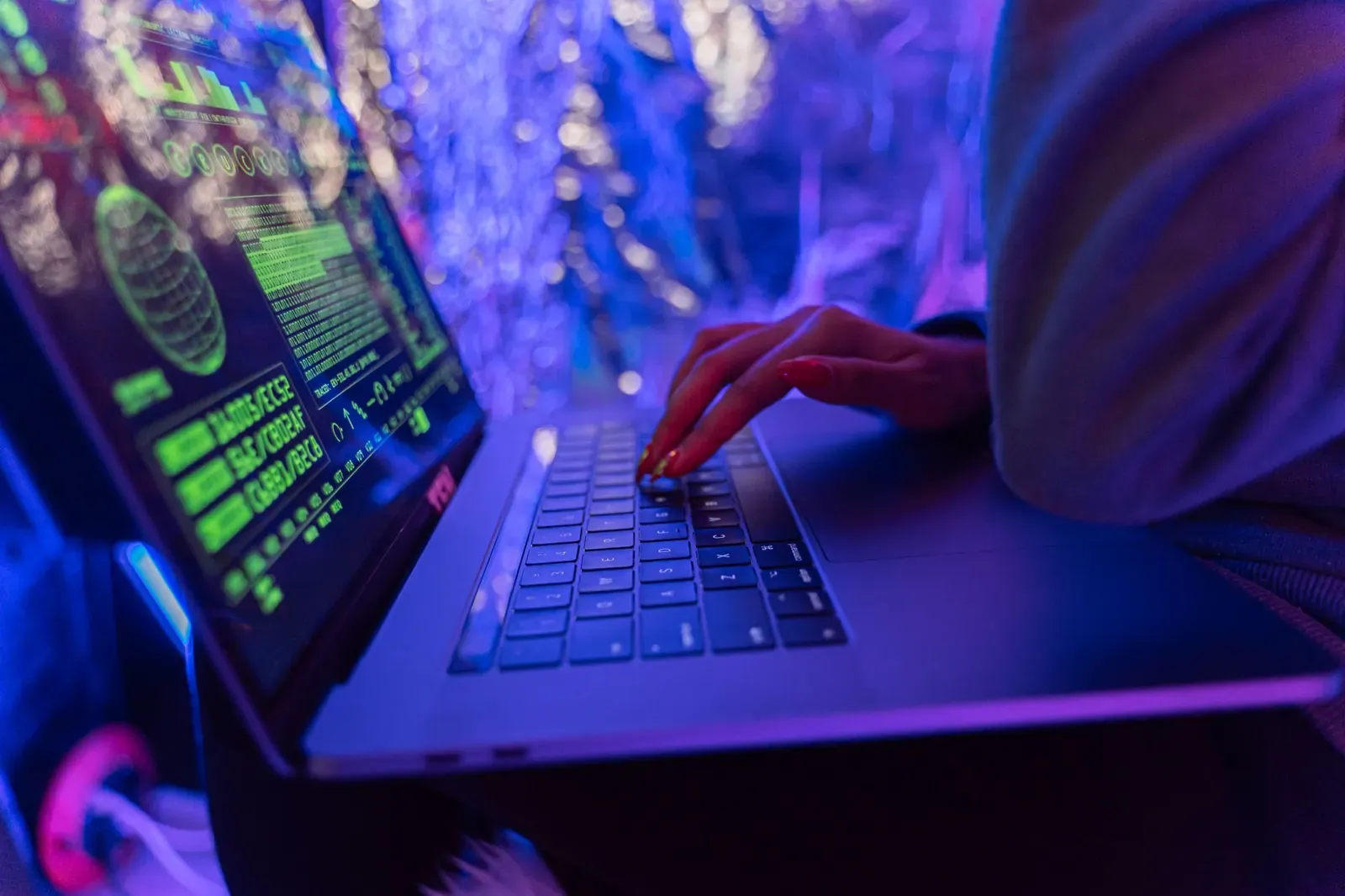 Gros plan des mains tapant sur un ordinateur portable affichant des graphiques de cybersécurité, éclairé par