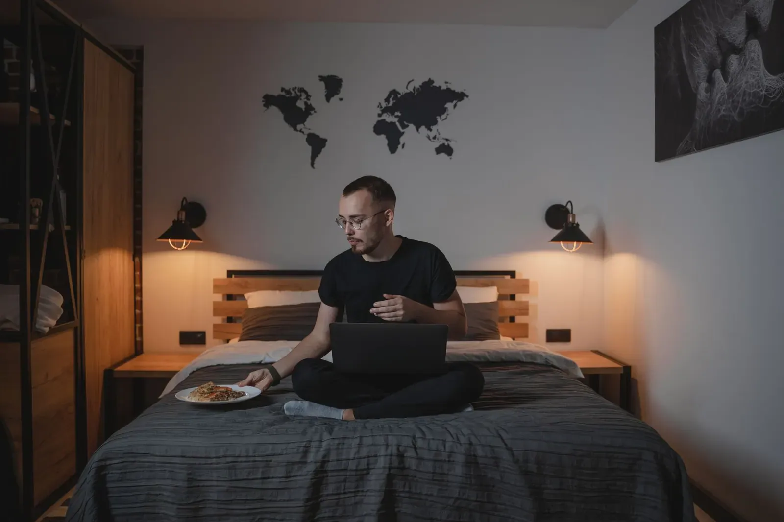 Un homme assis sur le lit d'une chambre d'hôtel, son ordinateur portable ouvert devant lui