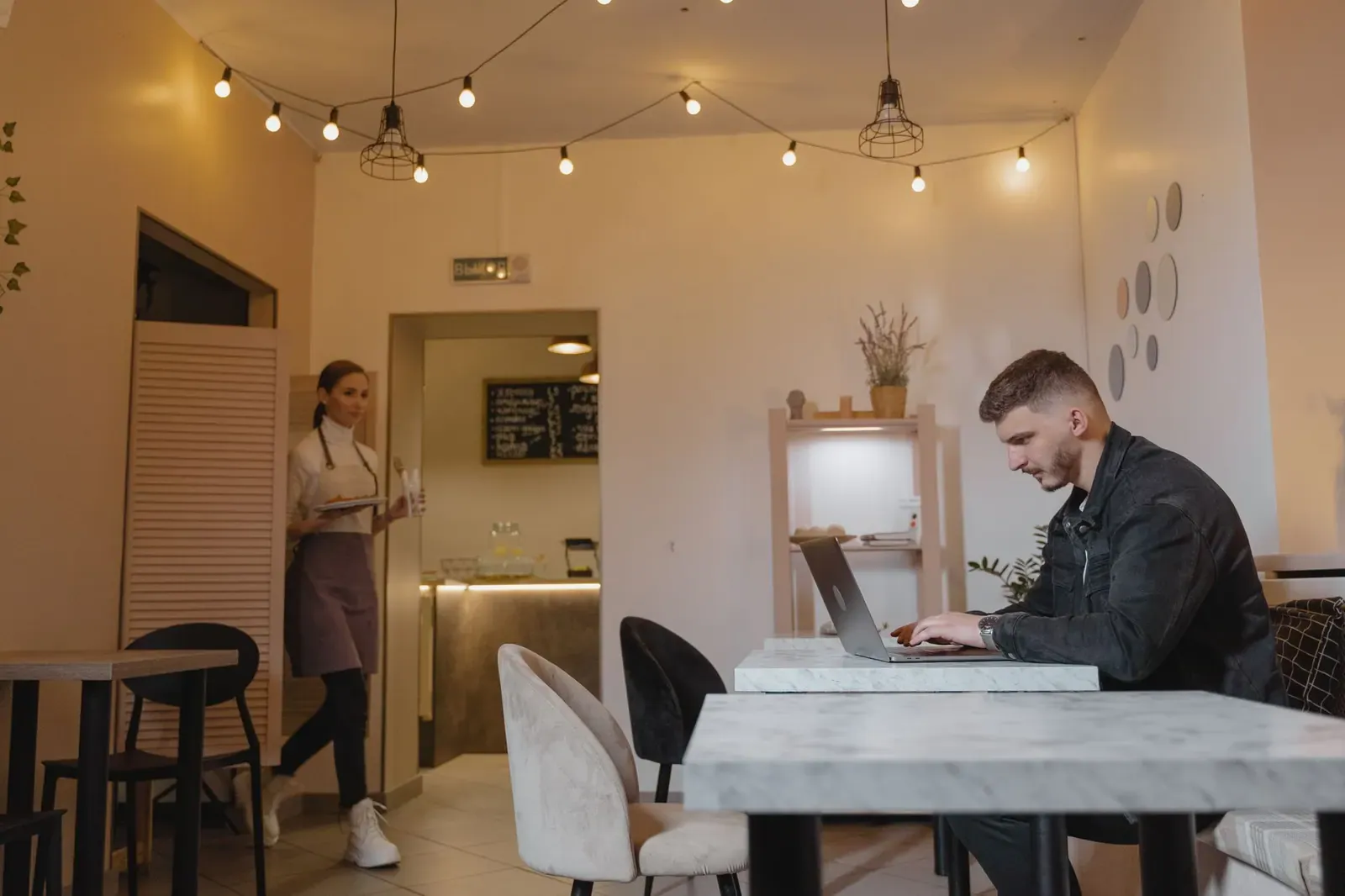 Homme travaillant sur un ordinateur portable dans un café élégant tandis qu'une serveuse sert les clients