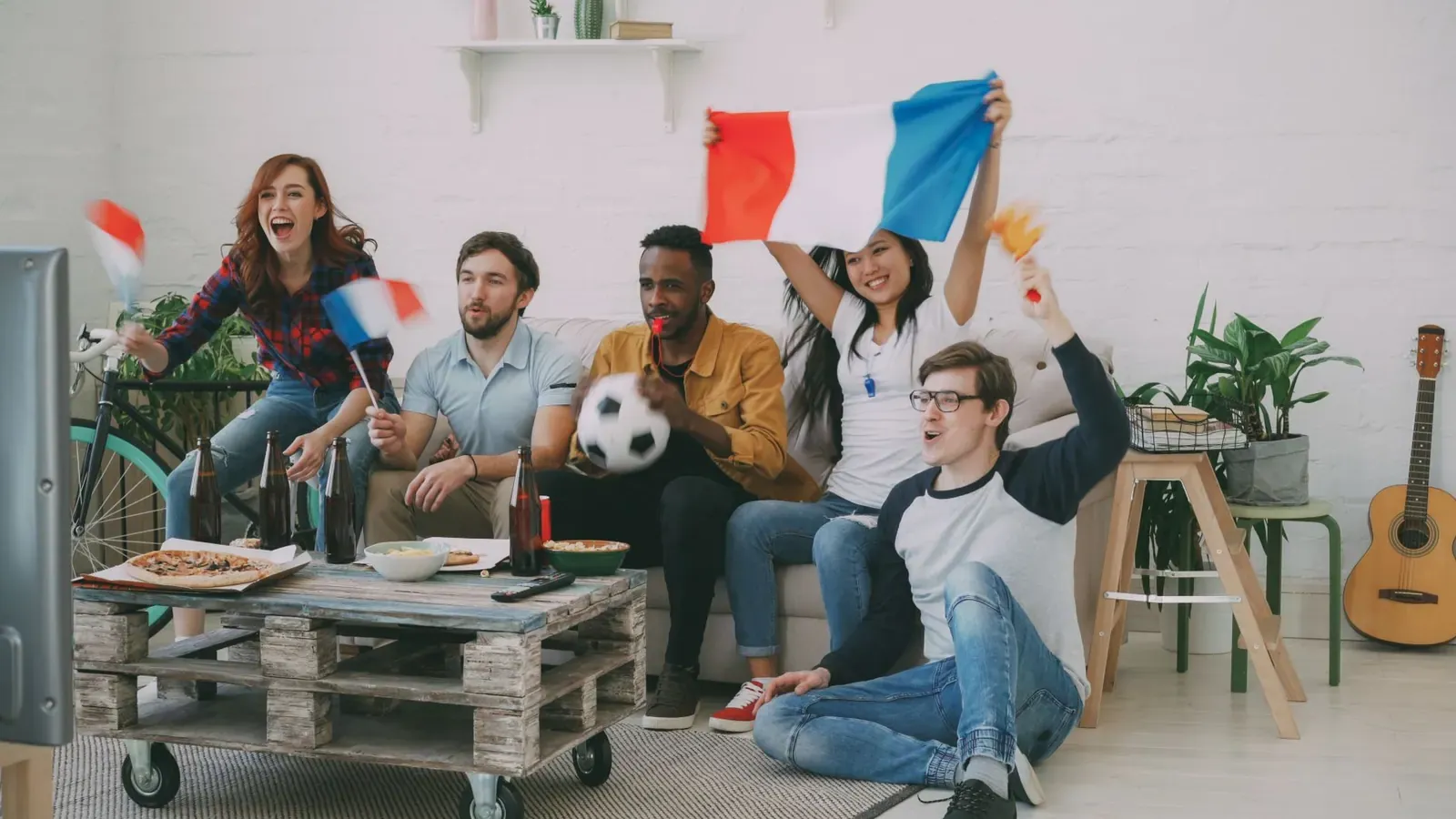 Des amis supporters, drapeau français en main, célèbrent un but devant la télévision