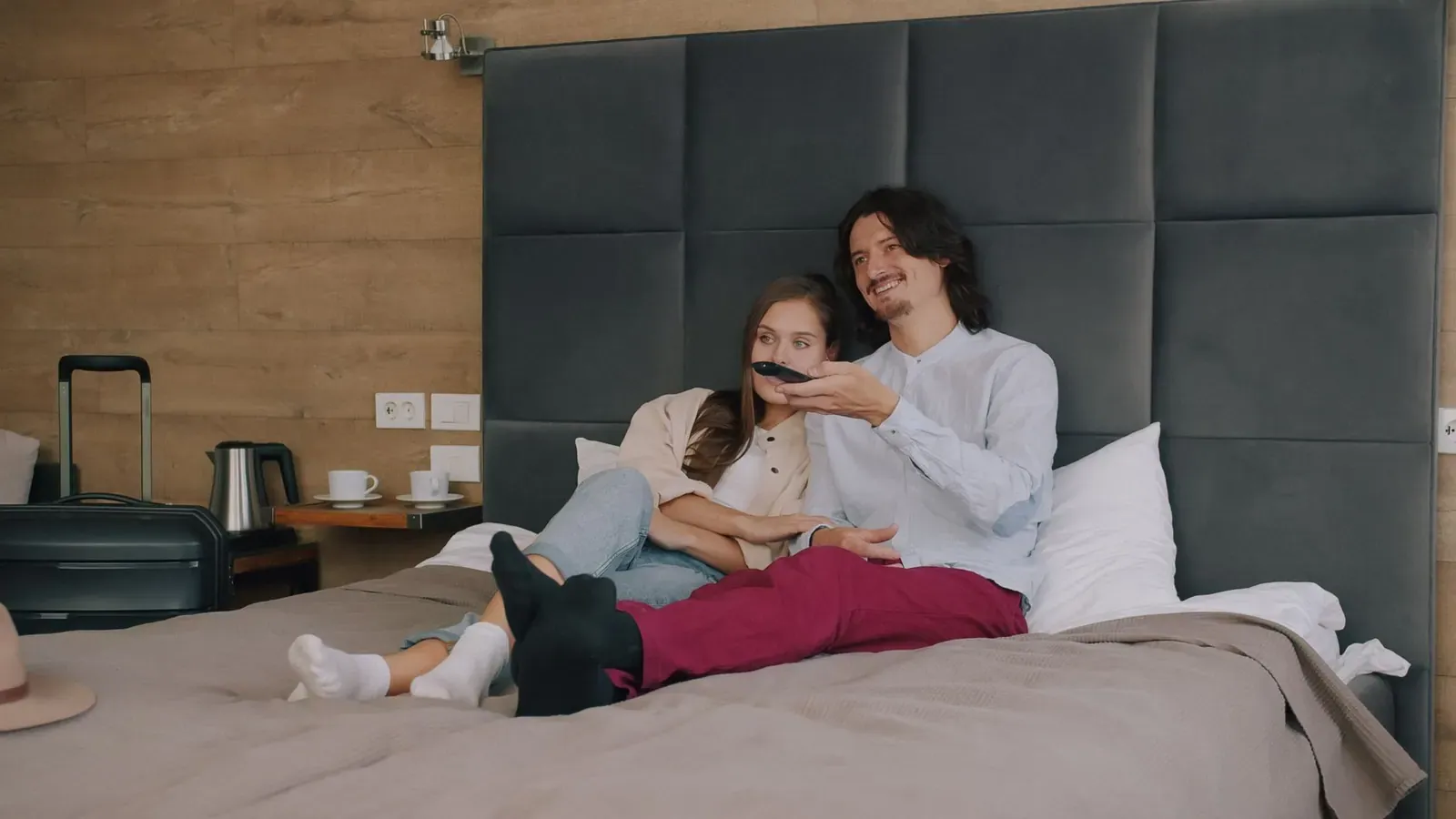 Un couple regarde la télévision depuis le lit d'une chambre d'hôtel