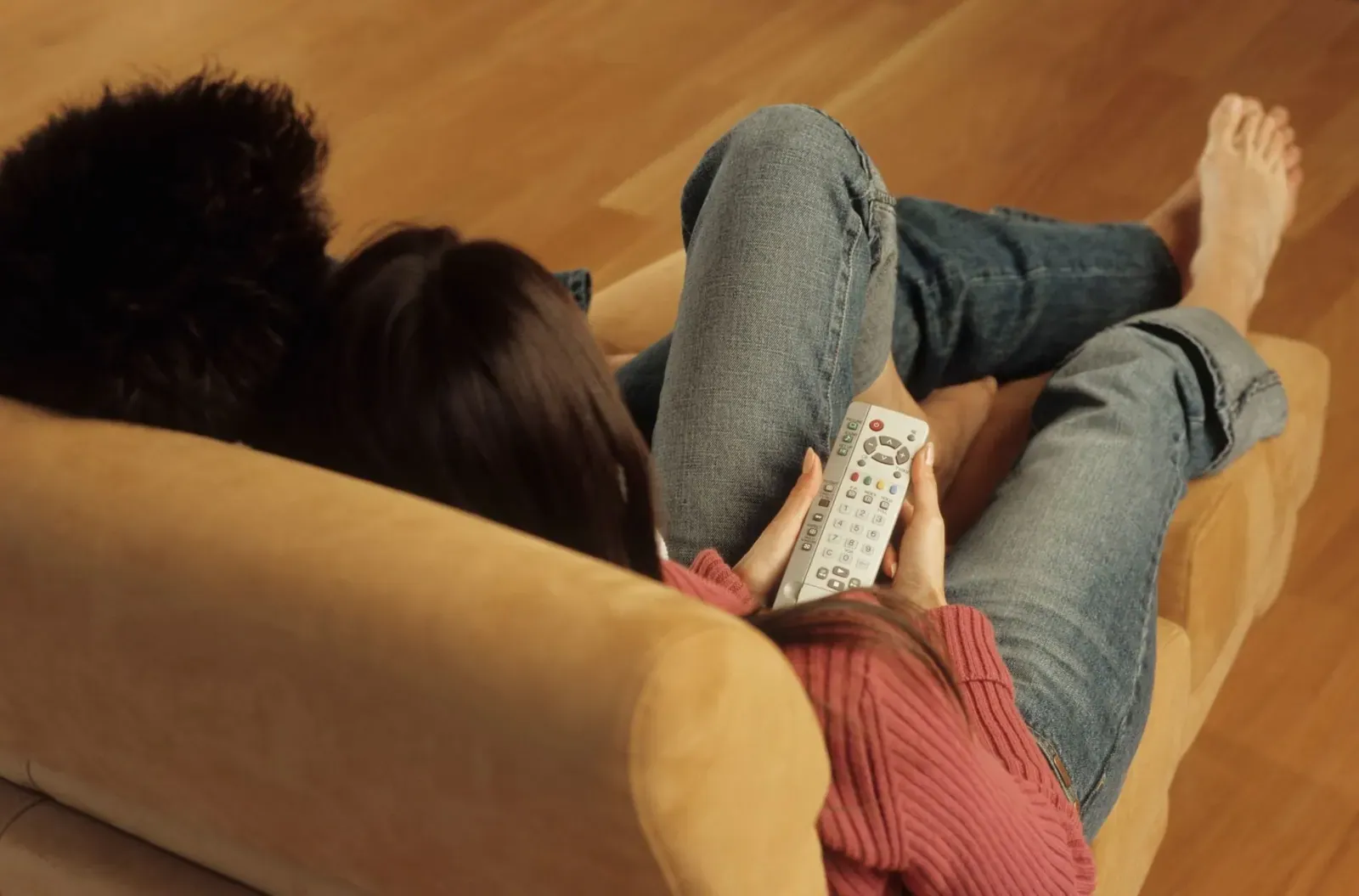 Une femme allongée sur un canapé tient une télécommande