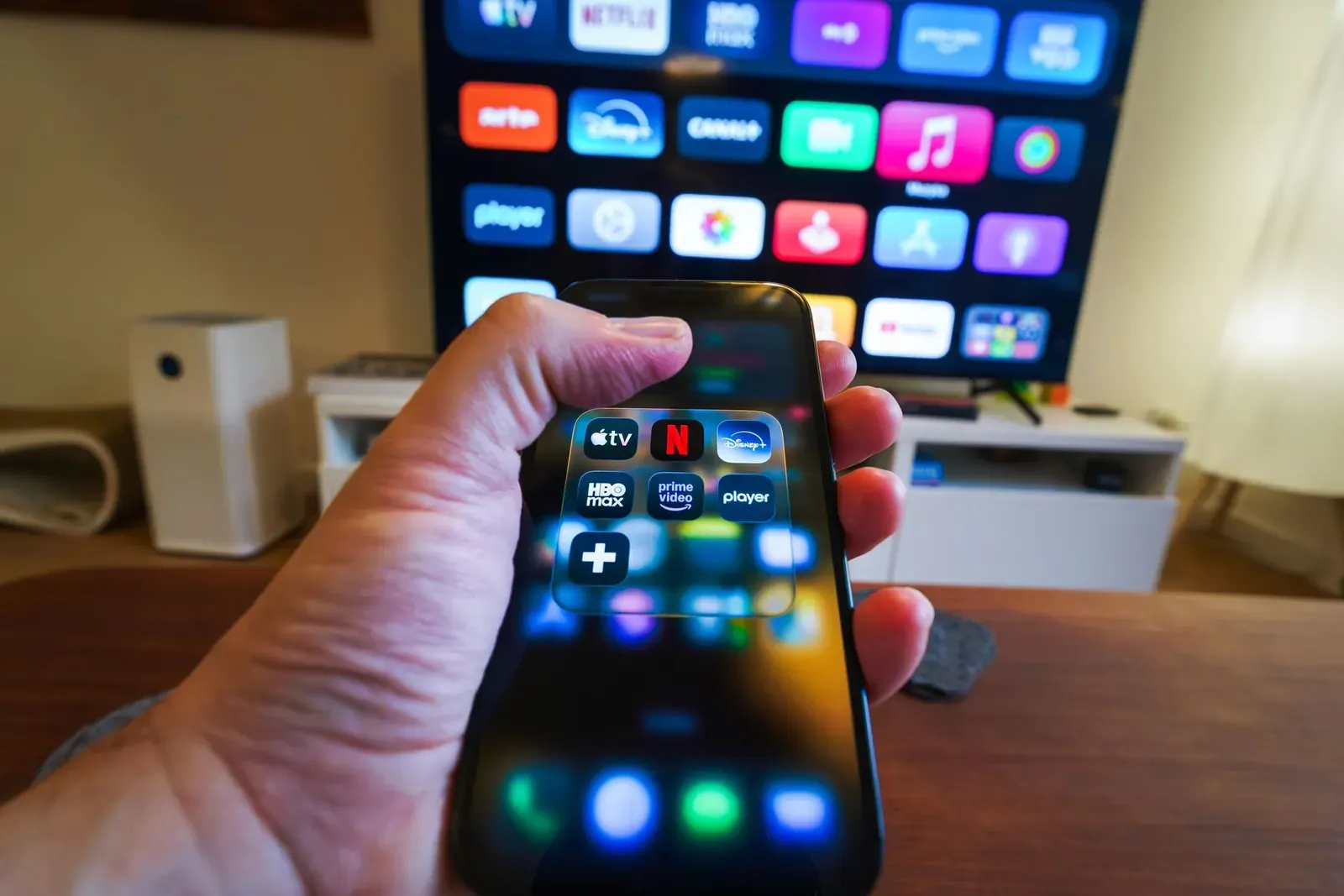Une main tient un smartphone devant un téléviseur qui affiche des applications de streaming