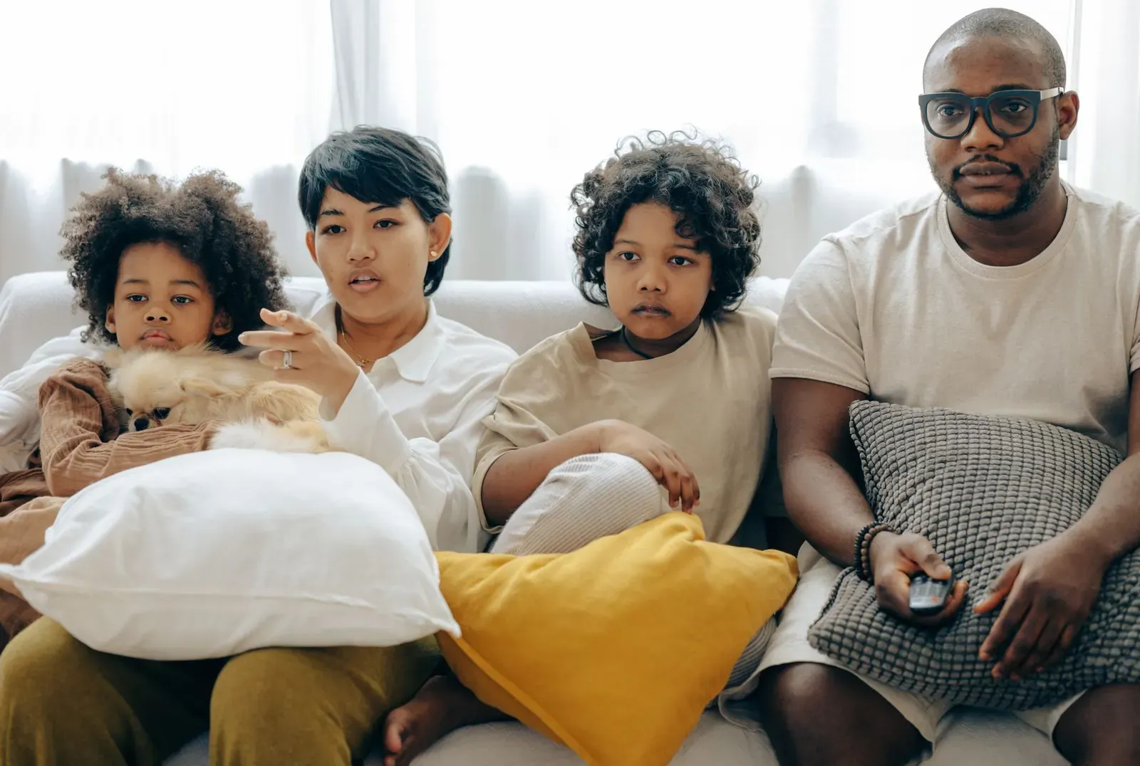 Une famille regarde la télévision, installée sur un canapé avec des coussins